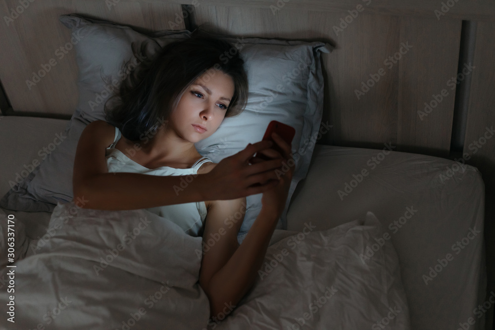 Female using smartphone in bed at night. Smartphone and social networks dependence. Insomia and harm of smartphone before going to bed. Female using smartphone in bed at night. Smartphone and social networks dependence. Insomia and harm of smartphone before going to bed.