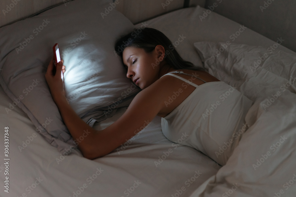 Sleeping woman is holding smartphone in her hand at night. Phone dependence and gadget overuse. Smartphone addiction Sleeping woman is holding smartphone in her hand at night. Phone dependence and gadget overuse. Smartphone addiction