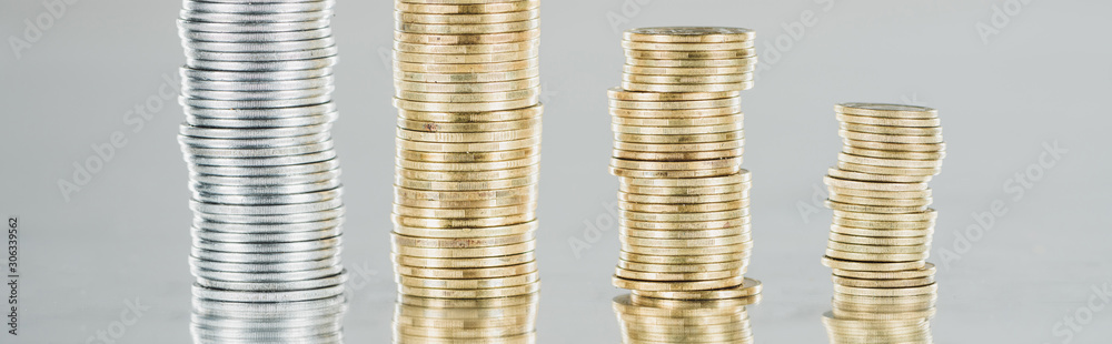 panoramic shot of stacked silver and golden coins on surface with reflection isolated on grey panoramic shot of stacked silver and golden coins on surface with reflection isolated on grey