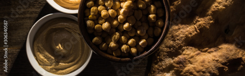 top view of delicious assorted hummus, chickpeas and fresh baked pita on wooden rustic table, panoramic shot