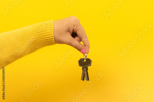 female hand holding house keys, suggesting, over yellow background photo