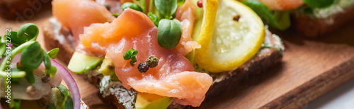 panoramic shot of salmon fillet near sliced lemon on tasty smorrebrod sandwich