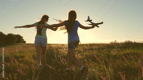 Happy childhood concept. Dreams of flying. Two girls play with toy plane at sunset. Children on background of sun with an airplane in hand. Silhouette of children playing on plane