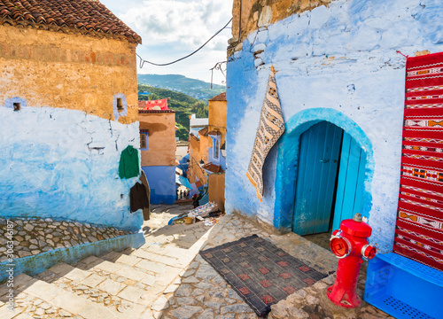 Beautiful street in Chefchaouen city in Morocco with bright walls and traditional carpets © leelook