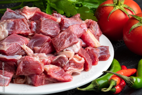 Pieces of raw meat on a white plate close-up with fresh vegetables