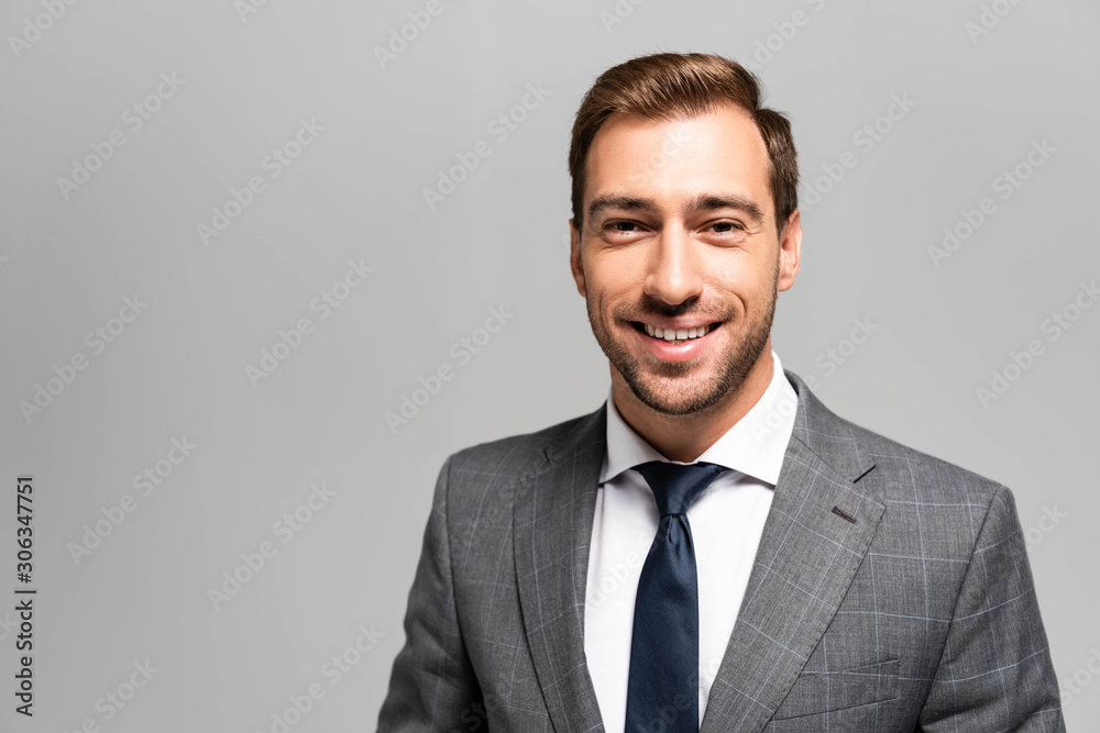 handsome and smiling businessman in suit looking at camera isolated on grey handsome and smiling businessman in suit looking at camera isolated on grey