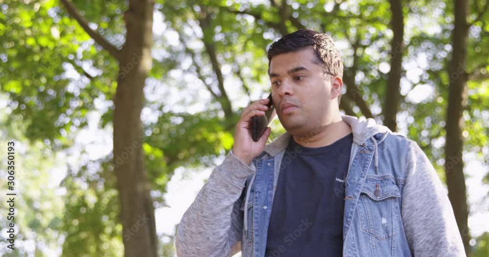 Indian man dials and begins a phone call while standing in the park - Slow Motion - shot on RED Indian man dials and begins a phone call while standing in the park - Slow Motion - shot on RED