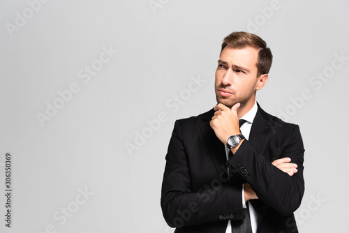 handsome and pensive businessman in suit looking up isolated on grey