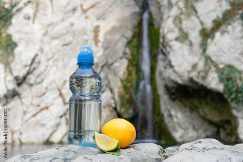 Schilderij op canvas Blue bottle with sport-lock lid lemon flavored, on the background of a waterfall