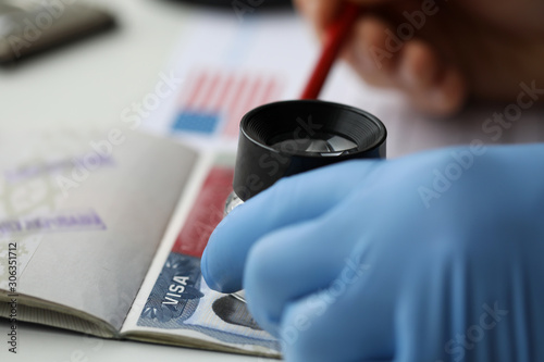 Fotografie Specialist with loupe checking authenticity of american visa in passport
