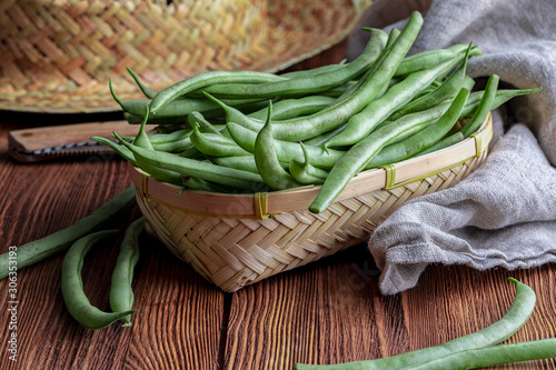 Fresh and raw green beans (green round beans) in wicker basket. Rustic and homemade look on wooden background.