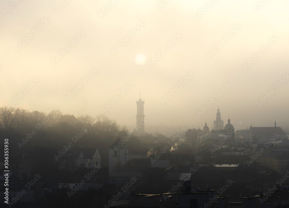 Historic center of Lviv in dense fog. Silhouette of the sun over the town hall. Ukraine