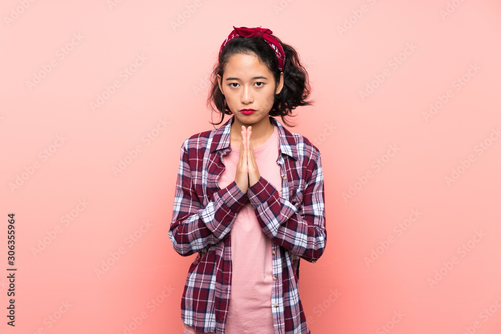 Asian young woman over isolated pink background keeps palm together. Person asks for something Asian young woman over isolated pink background keeps palm together. Person asks for something
