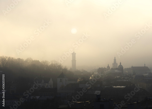 Historic center of Lviv in dense fog. Silhouette of the sun over the town hall. Ukraine