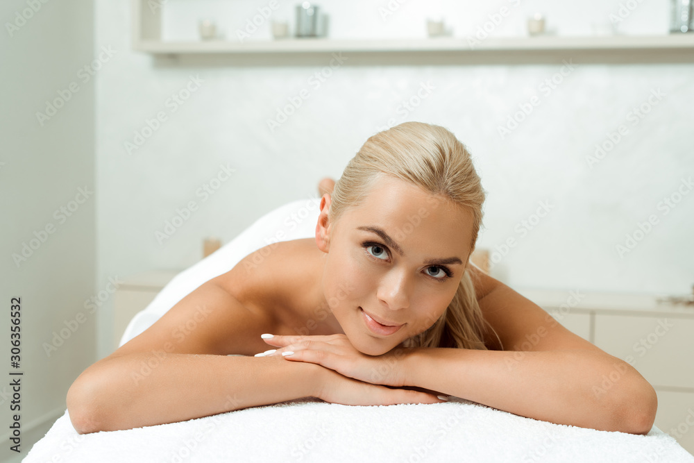 Naklejka premium attractive and smiling woman lying on massage table in spa