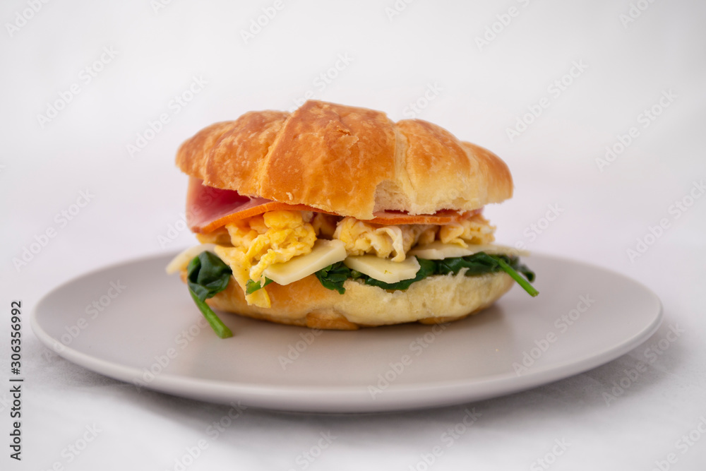 croissant sandwich of a ham, egg, spinach and avocado