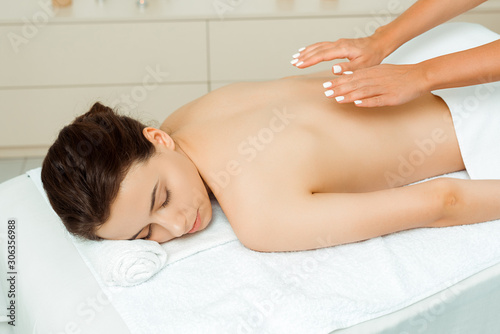 cropped view of masseur doing back massage to attractive woman in spa