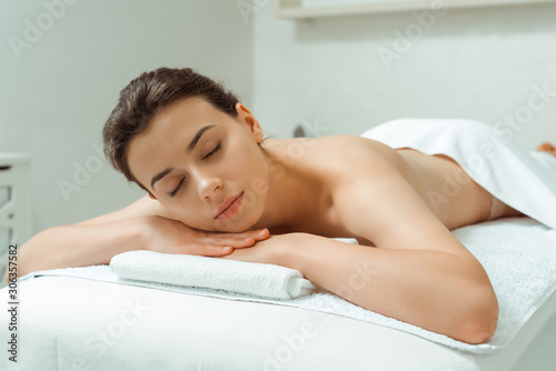 attractive woman with closed eyes lying on massage table in spa