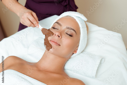 cropped view of cosmetologist applying face mask on attractive woman in spa