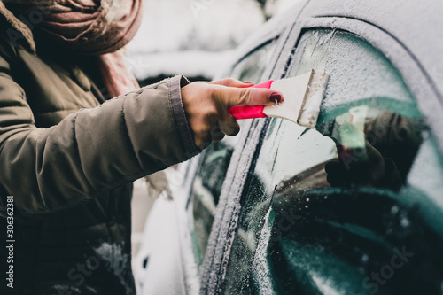 Hands of a woman seen cleaning a frosty window on a car. Early morning cleaning of iced car windows