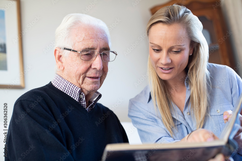 Grandfather Looking At Photo Album With Adult Granddaughter Grandfather Looking At Photo Album With Adult Granddaughter