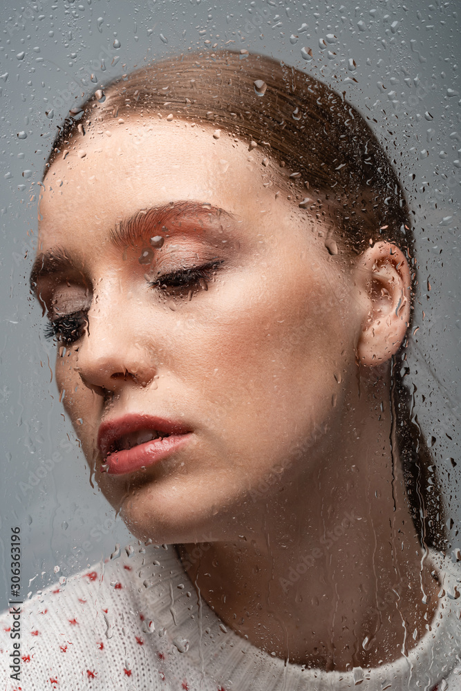 beautiful lonely woman on grey, beyond wet glass with drops