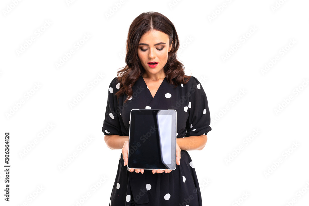 Young girl with delightful smile, in black and white dress in peas holds a tablet, picture isolated on white background Young girl with delightful smile, in black and white dress in peas holds a tablet, picture isolated on white background