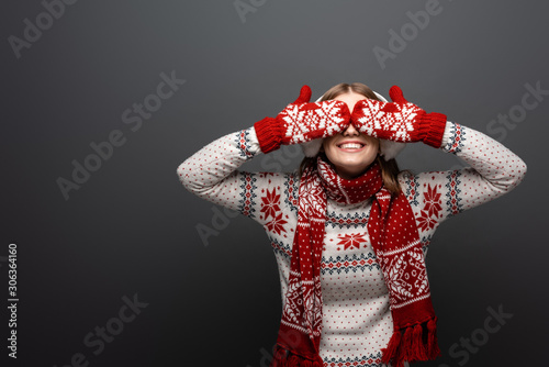 happy woman in christmas sweater, scarf, mittens and earmuffs closing eyes, isolated on grey