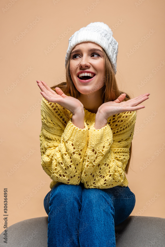 beautiful positive woman in yellow sweater and hat sitting on armchair, isolated on beige beautiful positive woman in yellow sweater and hat sitting on armchair, isolated on beige
