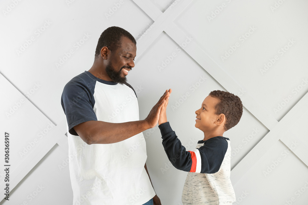 Obraz premium Portrait of African-American man and his little son giving each other high-five on light background