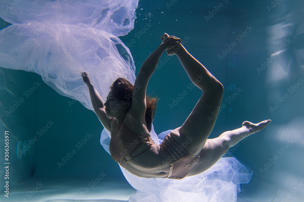 Fototapeta premium Beautiful girl gymnast and sportswoman swims underwater with shining fabric in the pool