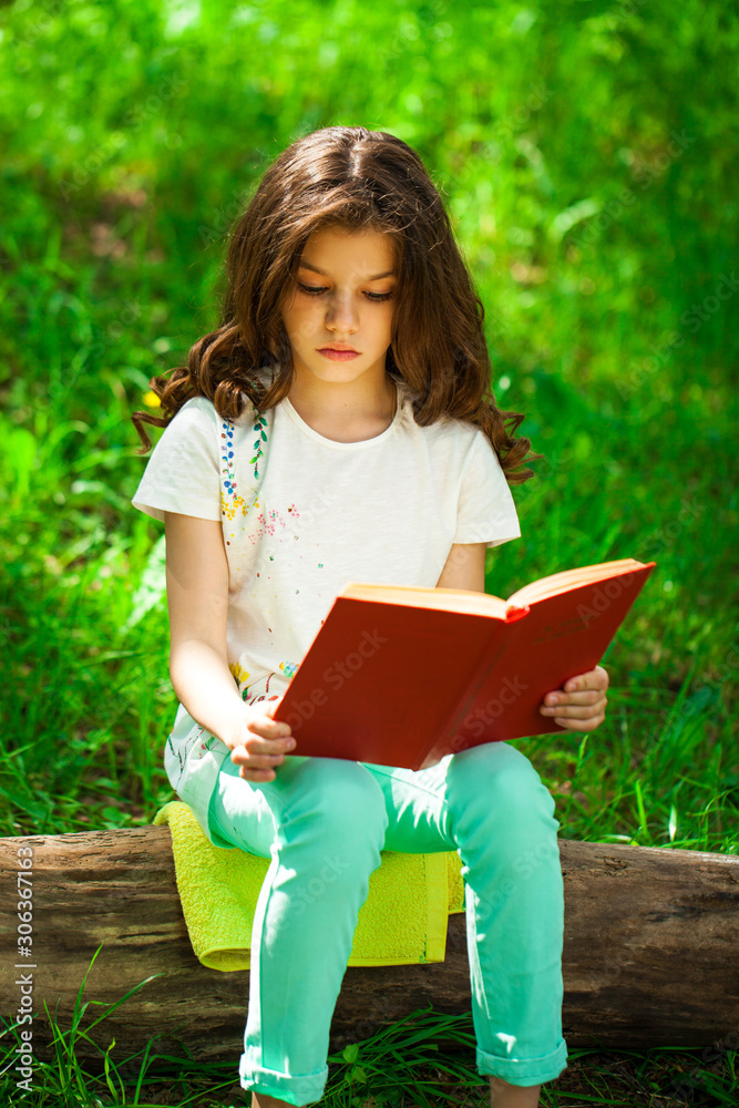 Charming little girl in forest with book sitting on tree stump Charming little girl in forest with book sitting on tree stump