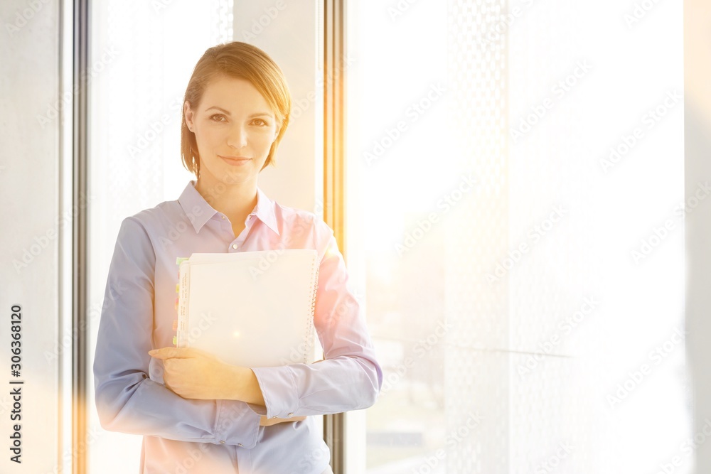 Portrait of businesswoman with file by window at office Portrait of businesswoman with file by window at office
