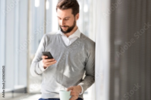 Businessman texting on mobile phone while having coffee at office