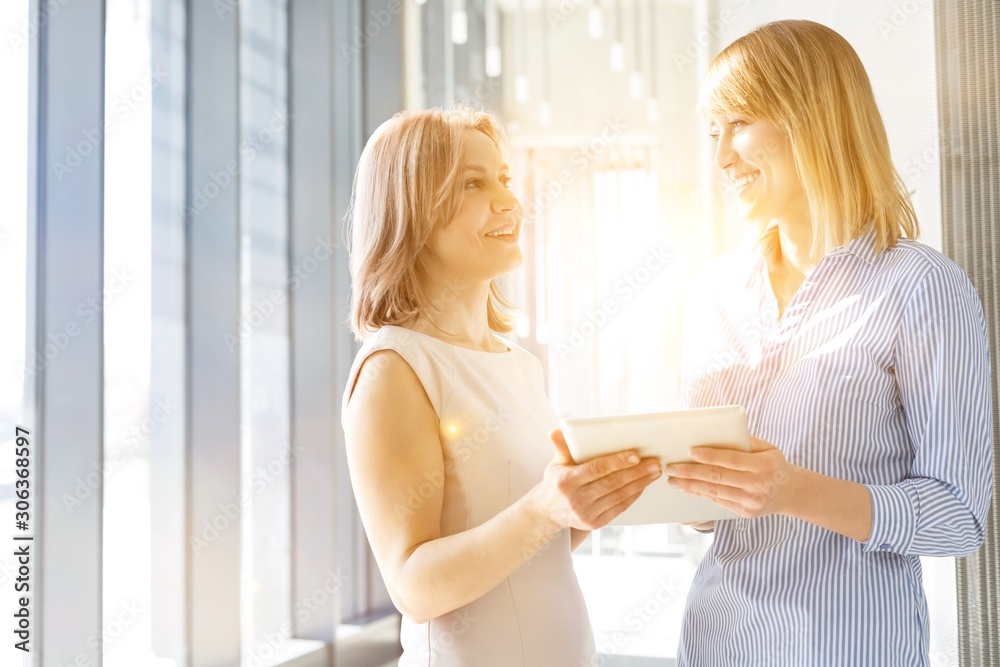 Businesswomen discussing over digital tablet in corridor at office