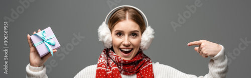Photos panoramic shot of excited girl in scarf and ear warmers pointing at christmas gi