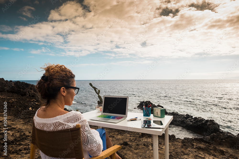 Obraz premium Modern and alternative lifestyle office wokstation with free business woman at work in open office with scenic ocean view - freedom from usual job - digital nomad life