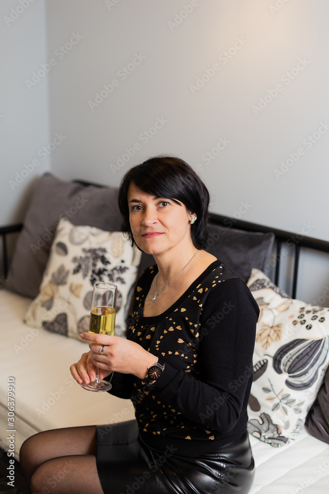 Beautiful woman 50 years old on a modern sofa with a glass of champagne in hand. Woman portrait. Beautiful woman 50 years old on a modern sofa with a glass of champagne in hand. Woman portrait.