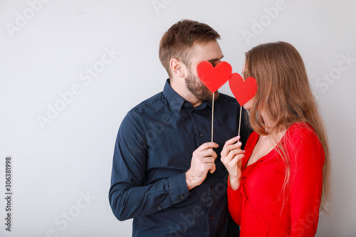 Happy young couple with red hearts on light background. Valentine's Day celebration