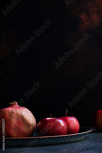 Still life of autumn red fruits, whole pomegranates and apples. Front view, black background, copy space