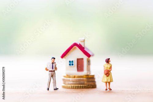 selective focus of miniature angry woman with miniature man and mini house on stack coins over blurred green garden background  for Asset management after divorce concept.