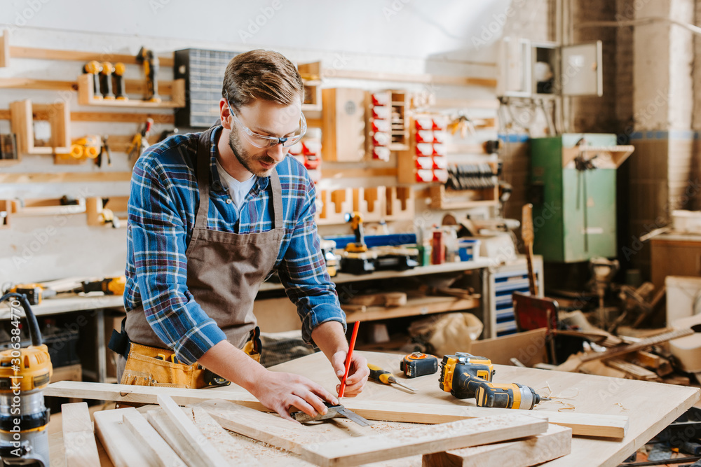 handsome carpenter in goggles holding pencil in carpentry shop handsome carpenter in goggles holding pencil in carpentry shop