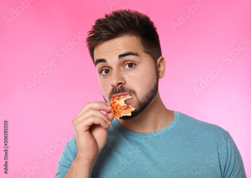 Emotional man eating pizza on pink background