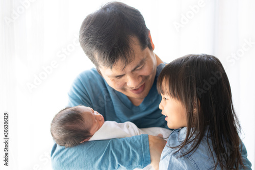 Asian young father is carrying his newborn baby boy and talking with his lovely daughter about her brother, concept of love and relation in family and bonding of the parent to their child, 