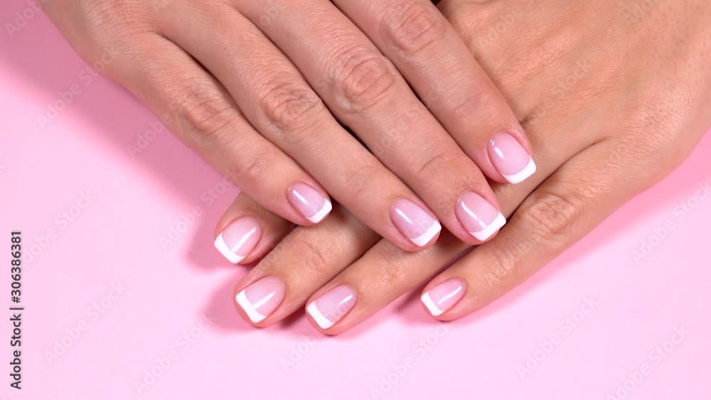Closeup top view of two beautiful female hands with elegant clasic professional fresh french pink and white manicure isolated on pastel pink background. Real time full hd video footage.