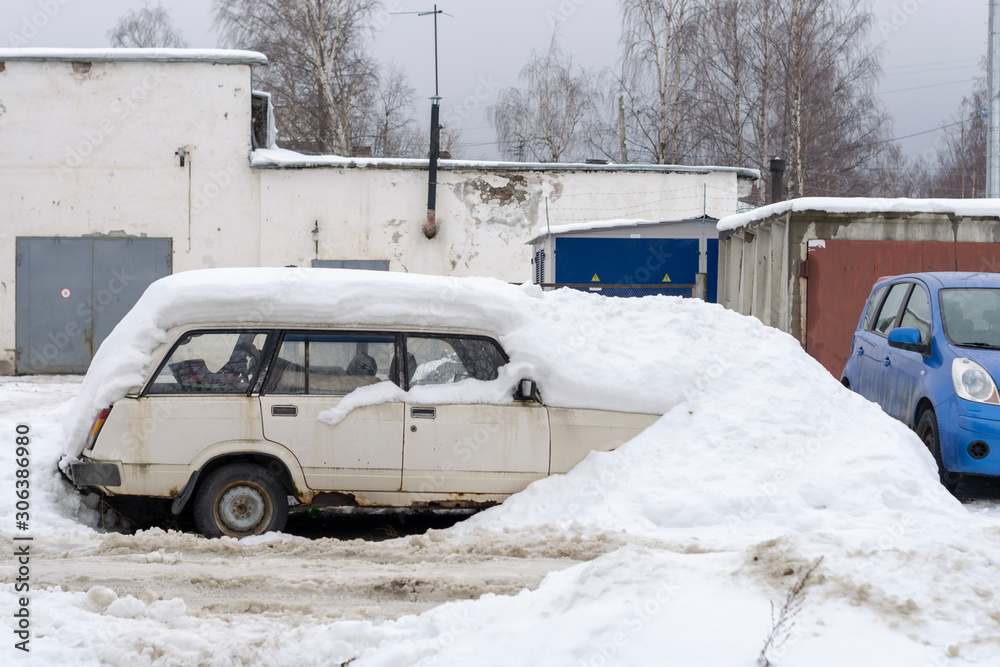 an old abandoned car is buried under a giant snowdrift.