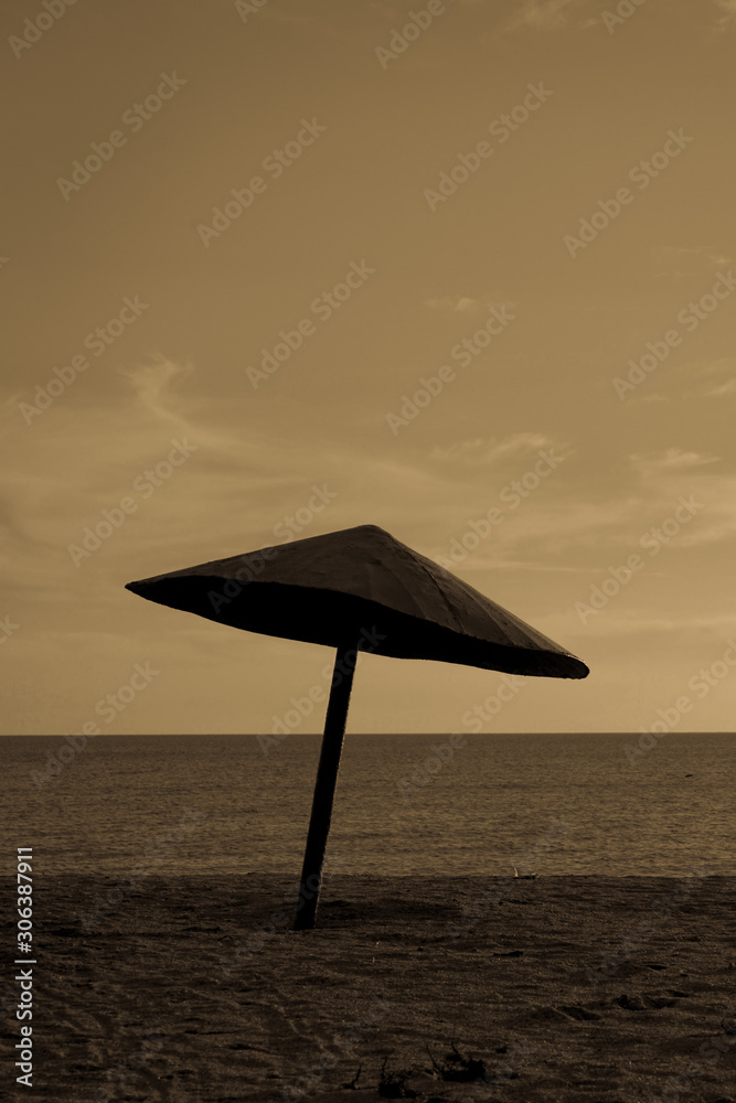 Umbrella on sandy beach in evening, sepia photo.