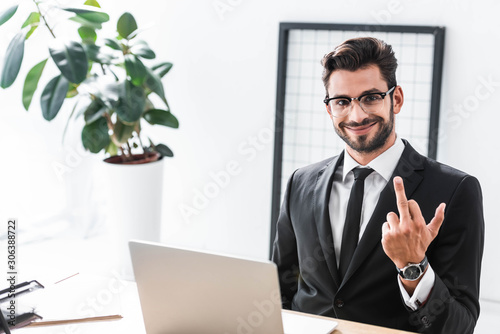 Handsome businessman looking at camera while using laptop