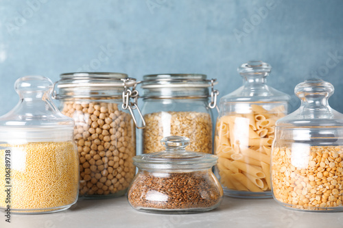 Jars with different cereals on grey marble table against light blue background