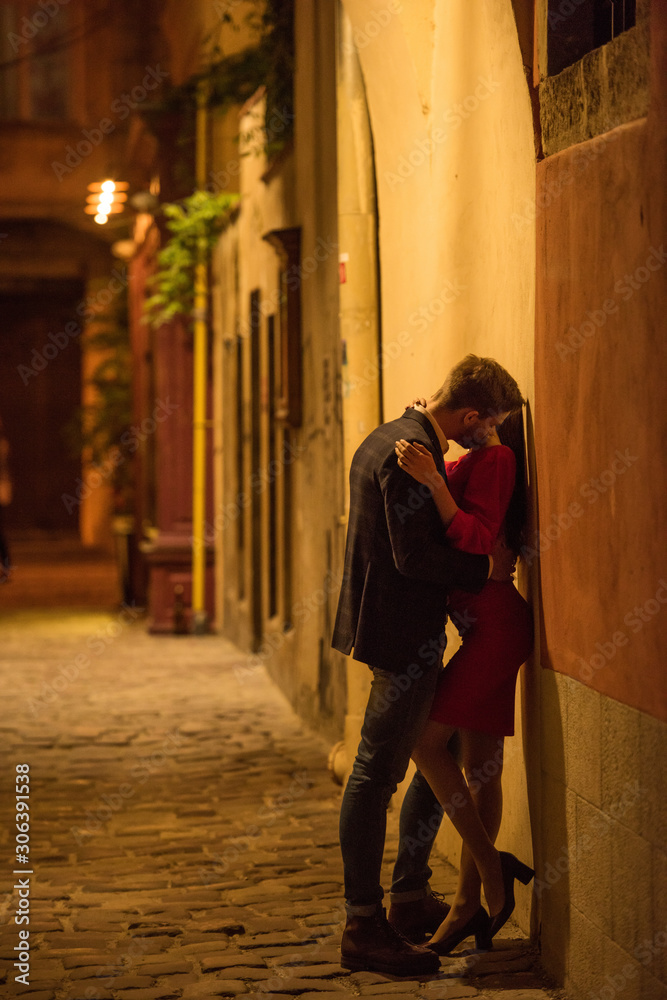 young couple embracing and kissing while standing near wall at night young couple embracing and kissing while standing near wall at night